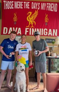 Julia, her nephews and Dava's dog Lennon stood in a living room, posing in front of a large Liverpool FC flag that reads "These were the days my friend. Dava Finnigan".