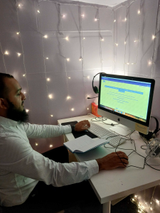 mysa mentor ali, in a shed getting his mentor portal ready on the computer to give a session to a member. the room is softly lit with fairy lights on the wall